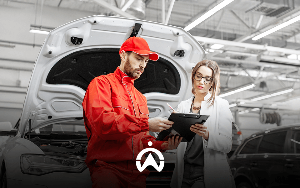 Mechanic in red uniform discussing car details with a client in a workshop.