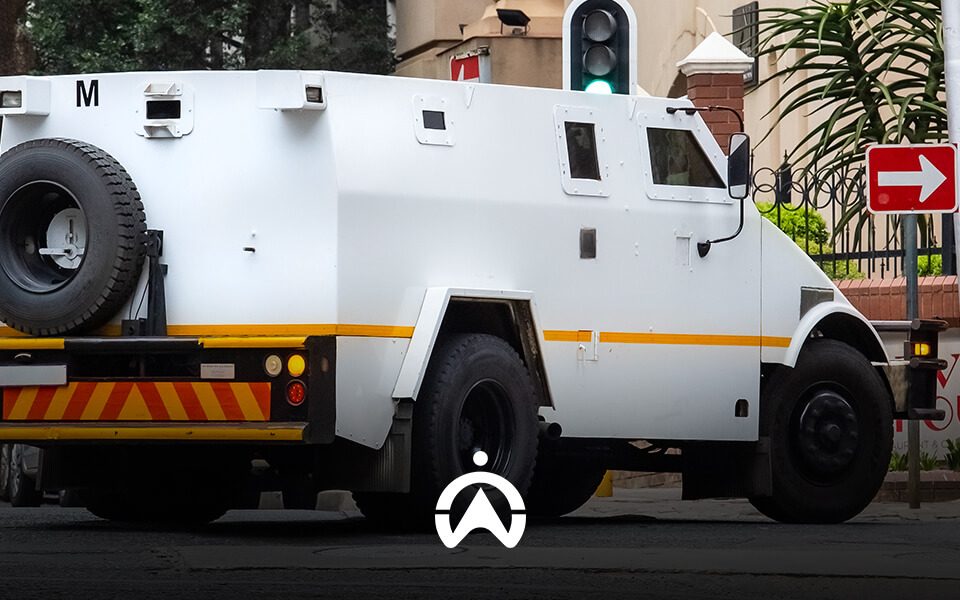 A white armored vehicle, marked with an "M," is parked at a traffic signal alongside a red right-turn sign.