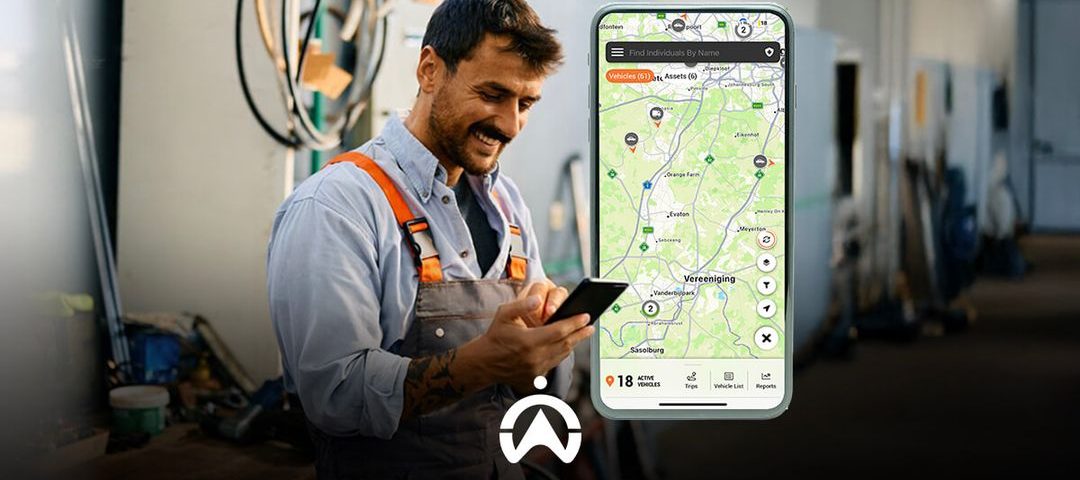 A professional in work attire reviews a mobile app displaying a map with vehicle locations and stats in a workshop environment.