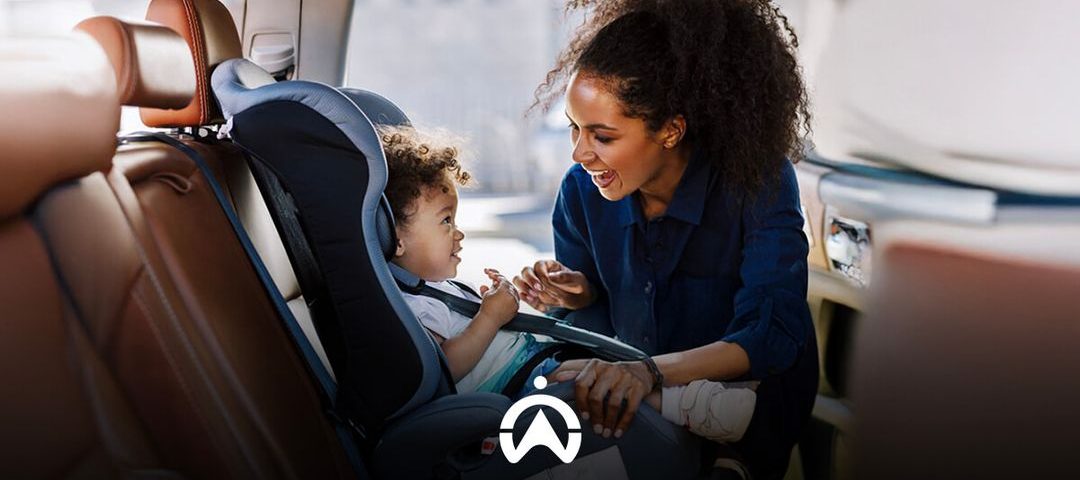 A woman interacts with a child securely seated in a car seat, surrounded by leather car interior, emphasizing safety and care.