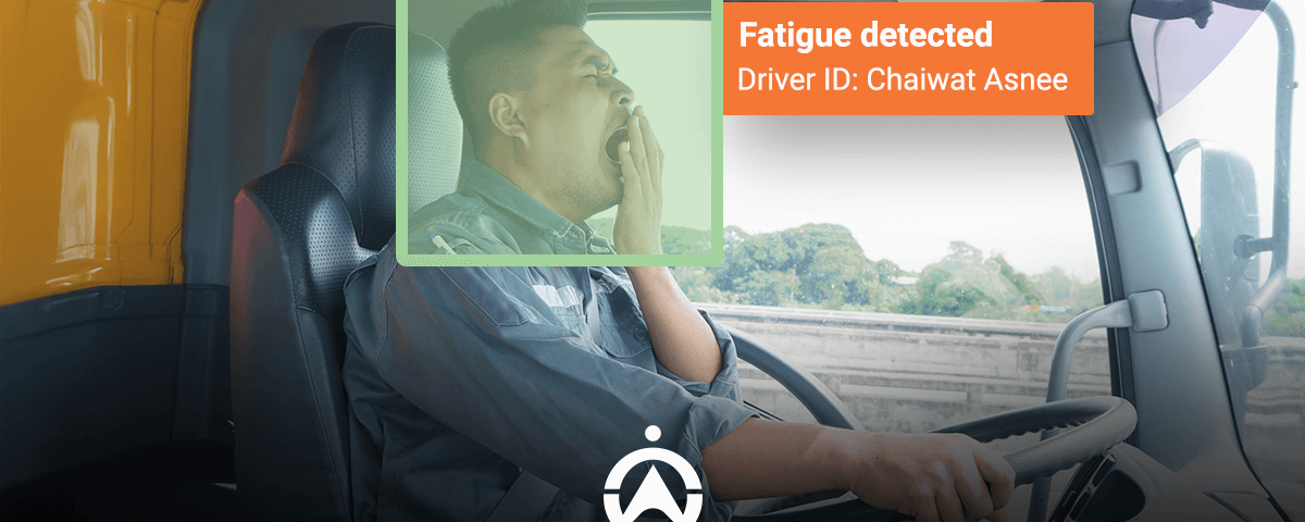 A truck driver rests his arm on the steering wheel while warnings about fatigue display on the screen in front of him.