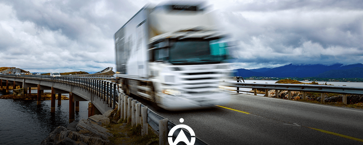 A white truck speeds across a bridge beside a calm body of water, under a cloudy sky, creating a sense of motion and travel.
