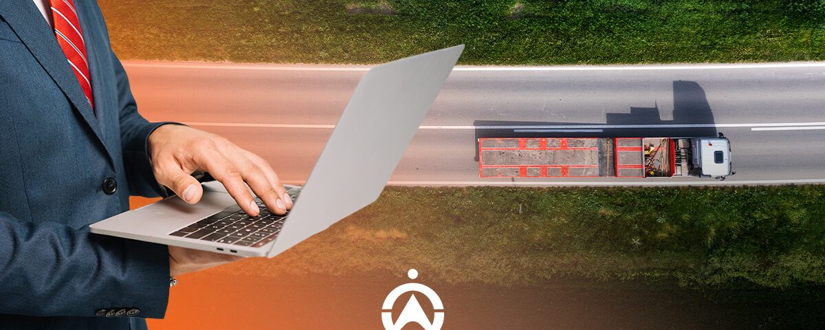 A businessman in a suit uses a laptop while a truck drives down a highway, symbolizing logistics and digital management.
