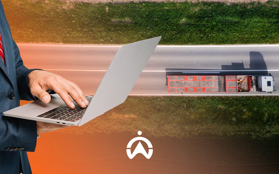A businessman in a suit uses a laptop while a truck drives down a highway, symbolizing logistics and digital management.