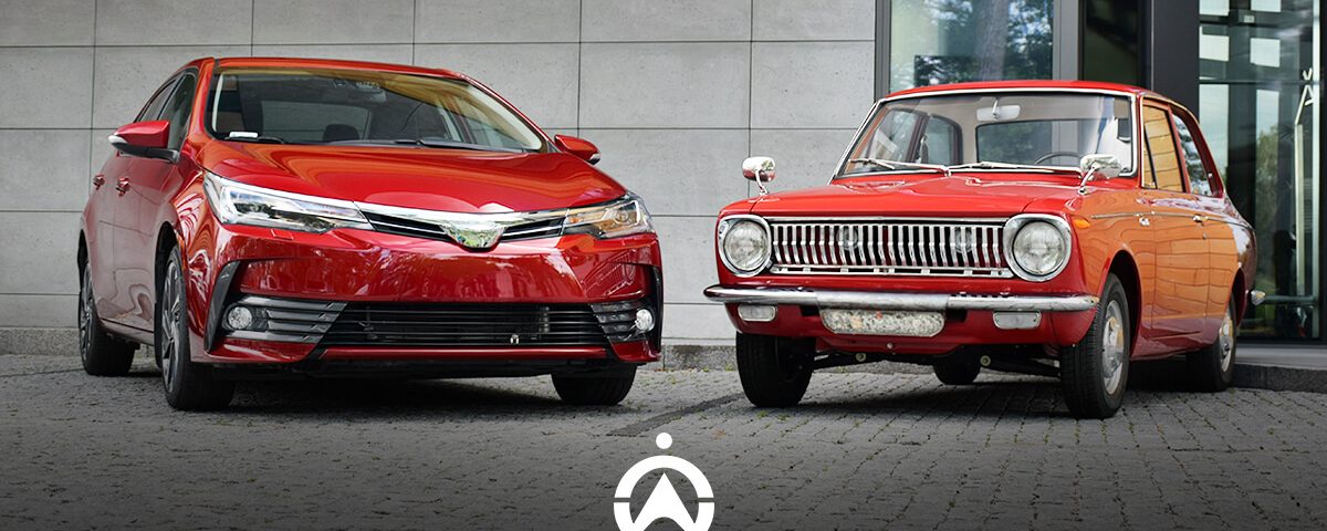A modern red sedan and a vintage red car parked side by side against a contemporary building backdrop.