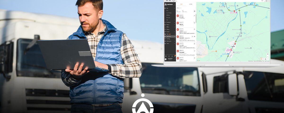 A man in a blue vest stands with a laptop, analyzing a map on the screen and surrounded by trucks in a parking area.